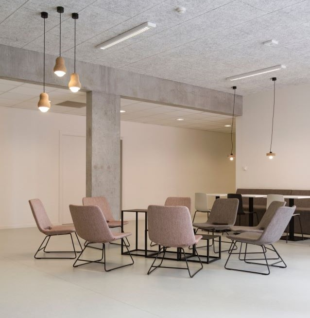 A group of beige chairs is centered in a plain-walled room with three lights hanging from the ceiling. Photo by Jean-Philippe Delberghe.